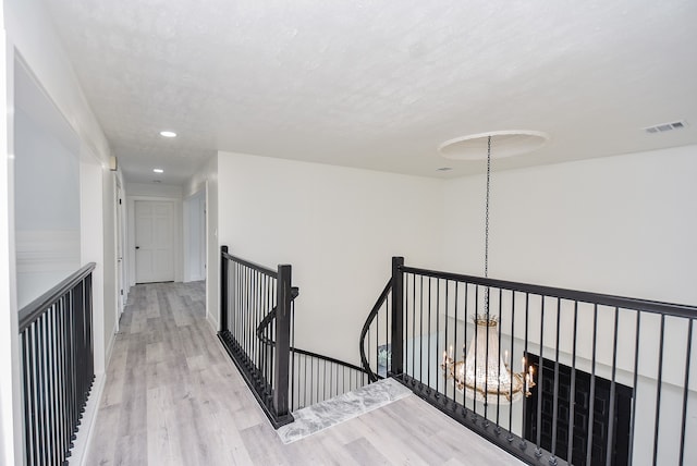 corridor with light wood-type flooring and a notable chandelier