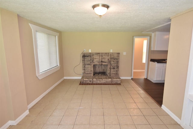 unfurnished living room featuring light tile patterned flooring, a brick fireplace, a textured ceiling, and baseboards