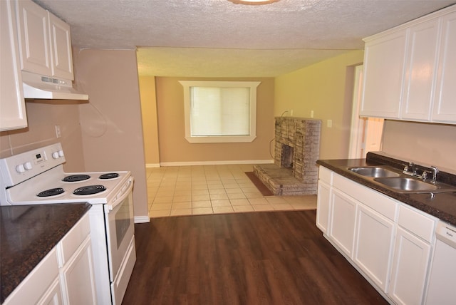 kitchen with under cabinet range hood, a sink, white appliances, white cabinets, and a fireplace