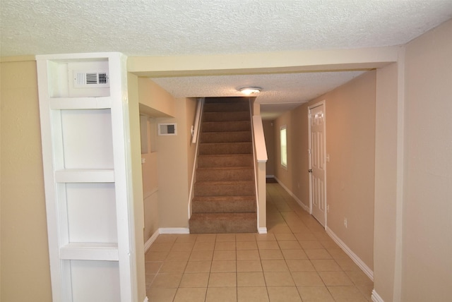 stairway featuring tile patterned floors, visible vents, a textured ceiling, and baseboards