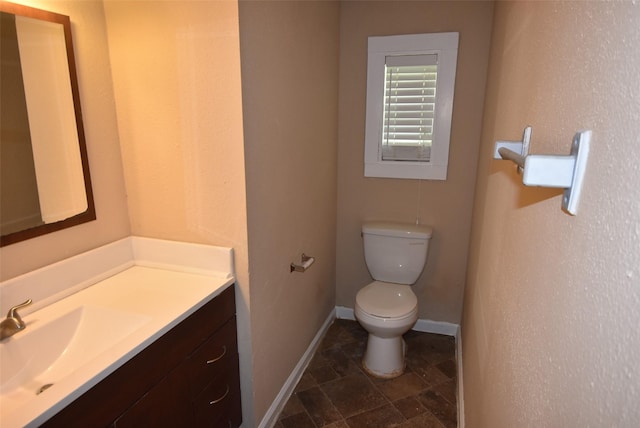 half bath with baseboards, toilet, vanity, and stone finish floor