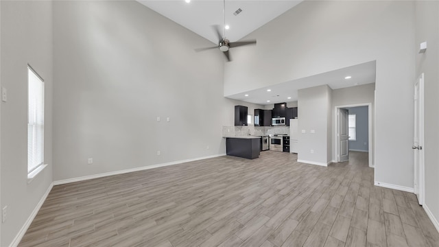 unfurnished living room featuring baseboards, a ceiling fan, a high ceiling, and light wood-style floors