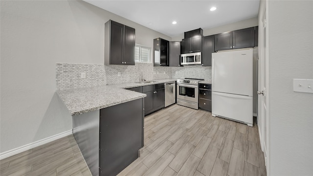 kitchen featuring light stone counters, a sink, decorative backsplash, a peninsula, and appliances with stainless steel finishes