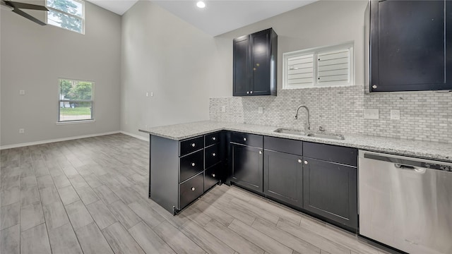 kitchen featuring a peninsula, stainless steel dishwasher, light stone countertops, and a sink