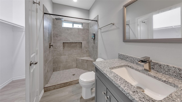 bathroom with a tile shower, wood finished floors, toilet, and vanity