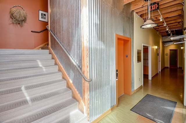 stairs featuring a towering ceiling, wood-type flooring, and beam ceiling