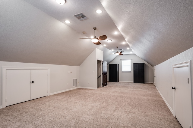 additional living space with lofted ceiling, ceiling fan, light colored carpet, and a textured ceiling