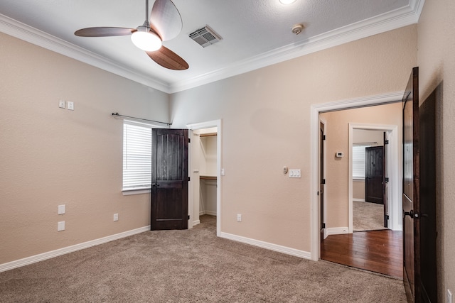 unfurnished bedroom featuring a spacious closet, ceiling fan, carpet flooring, and crown molding