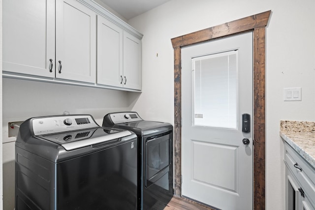 clothes washing area with washing machine and dryer, cabinets, and hardwood / wood-style flooring