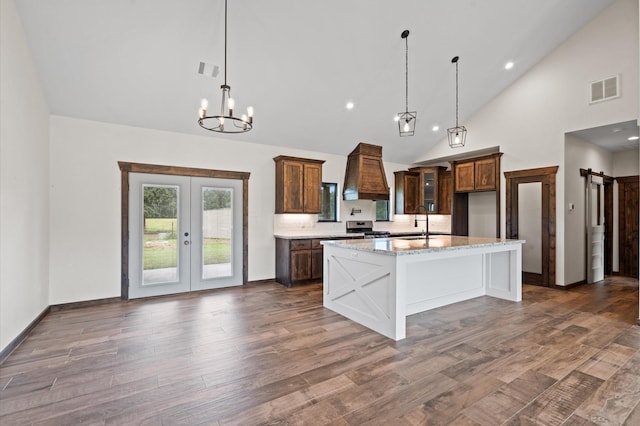 kitchen with light stone countertops, dark hardwood / wood-style flooring, stainless steel range oven, a kitchen island with sink, and custom exhaust hood