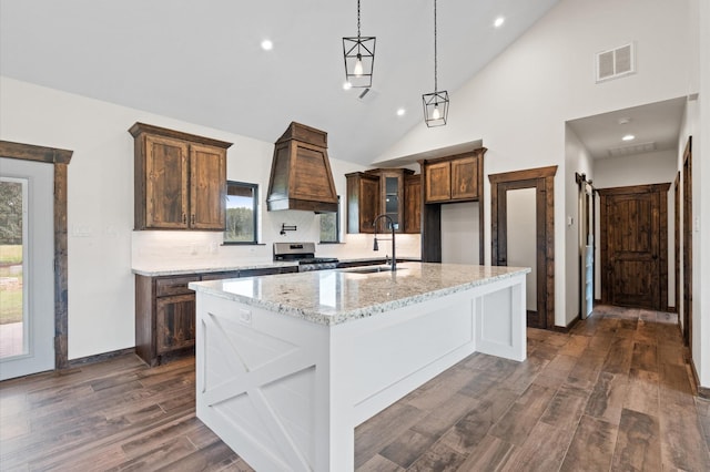 kitchen with light stone countertops, a barn door, high vaulted ceiling, stainless steel stove, and an island with sink