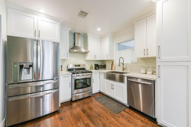 kitchen featuring sink, stainless steel appliances, wall chimney range hood, backsplash, and white cabinets