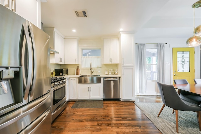 kitchen featuring appliances with stainless steel finishes, backsplash, sink, decorative light fixtures, and white cabinetry