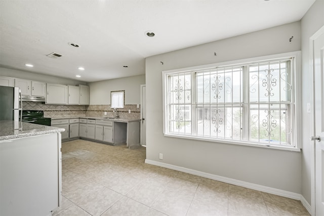 kitchen with sink, stainless steel refrigerator, decorative backsplash, light stone countertops, and black / electric stove