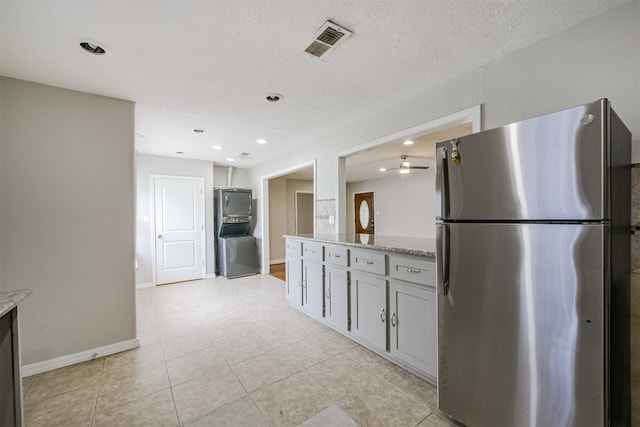 kitchen featuring a textured ceiling, light stone counters, ceiling fan, and stainless steel refrigerator