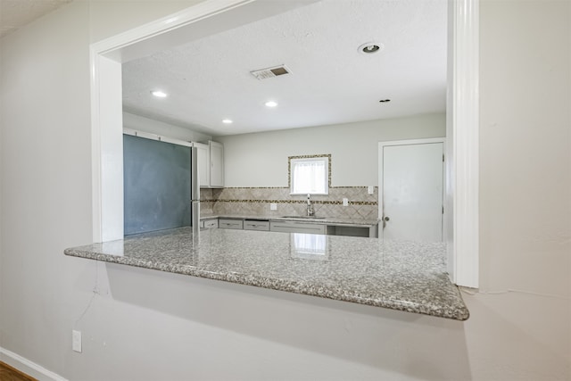 kitchen with kitchen peninsula, sink, tasteful backsplash, stainless steel refrigerator, and light stone countertops