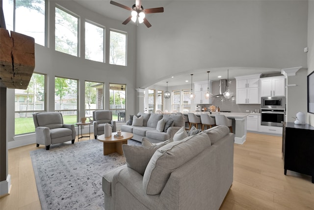 living room featuring a towering ceiling, ceiling fan, and light hardwood / wood-style flooring