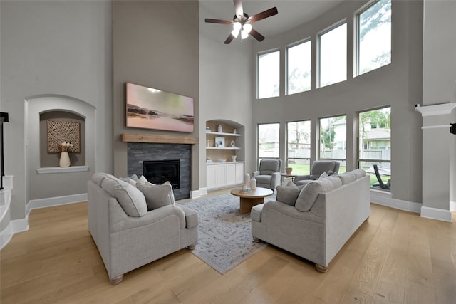 living room featuring built in shelves, light hardwood / wood-style flooring, ceiling fan, and a high ceiling