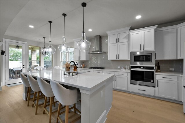 kitchen with white cabinets, appliances with stainless steel finishes, wall chimney exhaust hood, and a kitchen island with sink