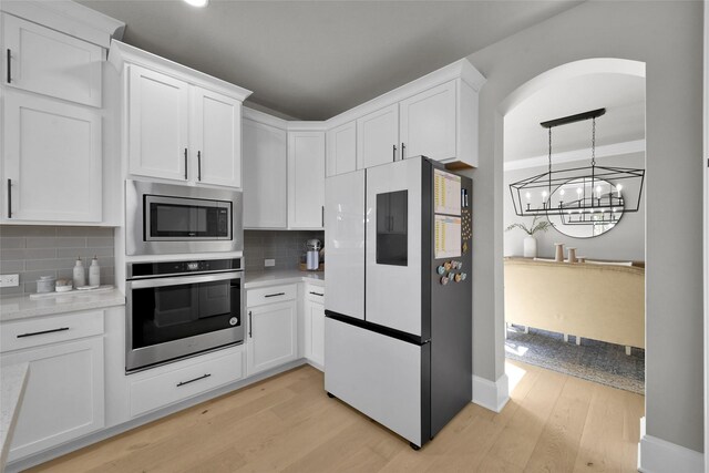 kitchen featuring light hardwood / wood-style flooring, appliances with stainless steel finishes, decorative backsplash, a chandelier, and white cabinetry