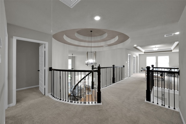 hallway featuring a raised ceiling, an inviting chandelier, and light carpet