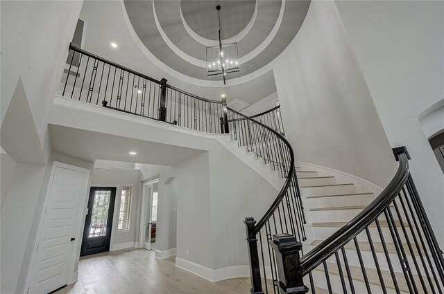 stairway with a tray ceiling, wood-type flooring, a chandelier, and a high ceiling