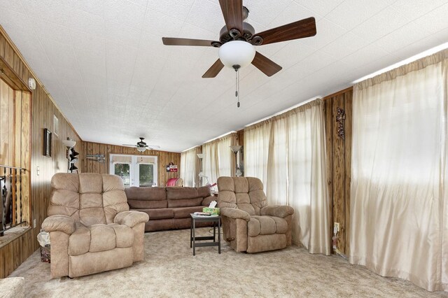 carpeted living room with ceiling fan and wooden walls