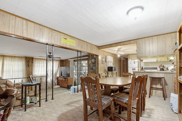 dining room with light colored carpet, ceiling fan, and wooden walls