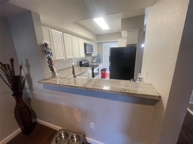 kitchen featuring tasteful backsplash, white cabinets, black fridge, stainless steel electric stove, and kitchen peninsula