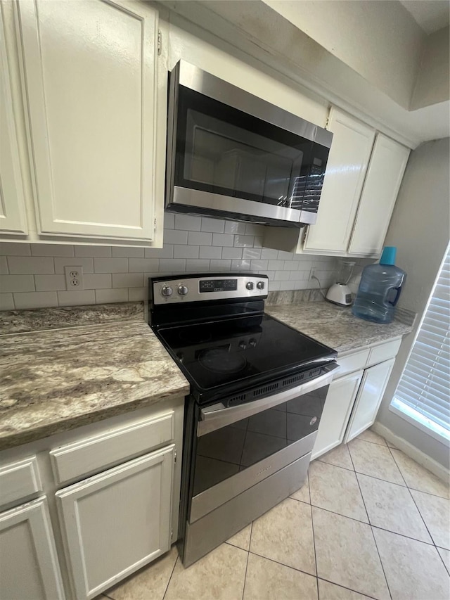 kitchen featuring appliances with stainless steel finishes, light tile patterned floors, white cabinets, and backsplash