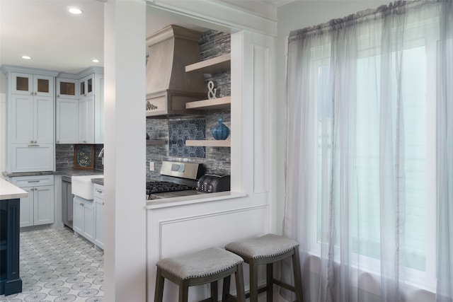 kitchen with sink, backsplash, stainless steel range oven, a kitchen breakfast bar, and white cabinetry