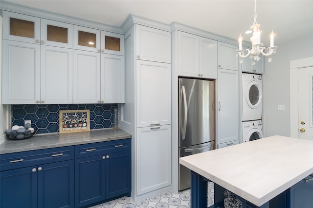 kitchen with stainless steel fridge, white cabinets, stacked washer and dryer, decorative light fixtures, and blue cabinets