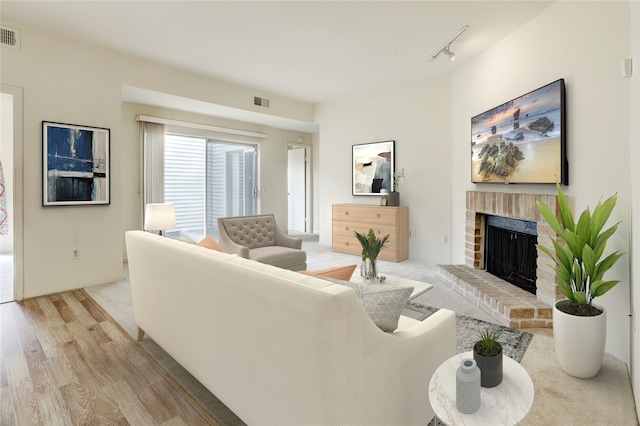 living room with light wood-type flooring, rail lighting, a fireplace, and visible vents