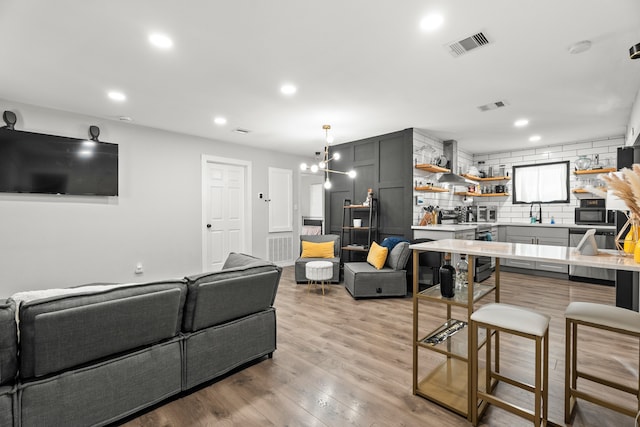 living room featuring a notable chandelier, sink, and light hardwood / wood-style flooring