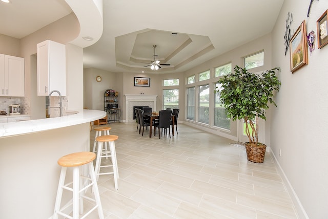 dining space featuring a tray ceiling, ceiling fan, sink, and a healthy amount of sunlight