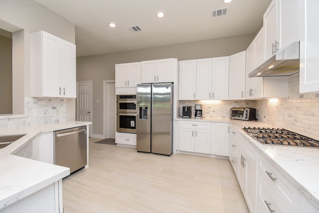 kitchen with backsplash, light stone counters, stainless steel appliances, and white cabinets