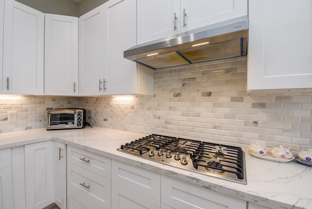 kitchen with stainless steel gas cooktop, light stone countertops, white cabinets, and decorative backsplash