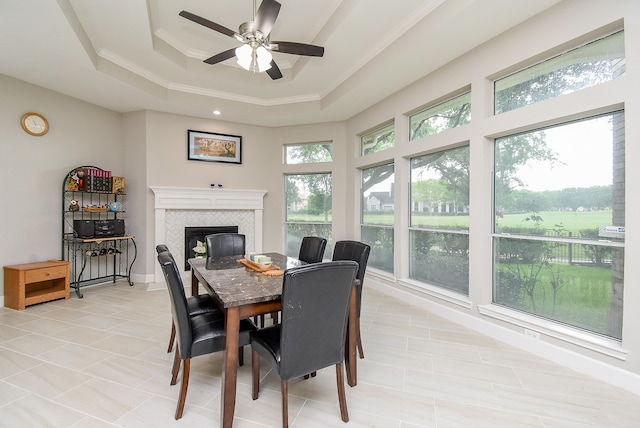 tiled dining room featuring a healthy amount of sunlight, ceiling fan, a raised ceiling, and a tile fireplace