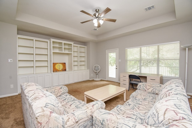 living room featuring a raised ceiling, ceiling fan, and light colored carpet