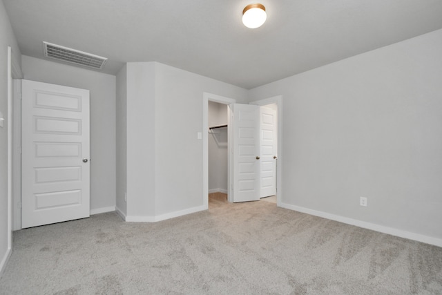 unfurnished bedroom with a walk in closet, light carpet, and a closet