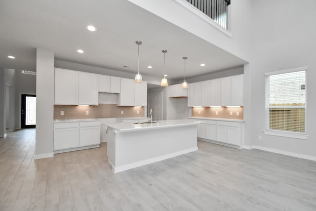 kitchen with backsplash, white cabinetry, an island with sink, and light wood-type flooring