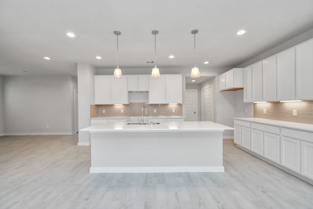 kitchen featuring white cabinets, a center island with sink, sink, decorative light fixtures, and light hardwood / wood-style floors