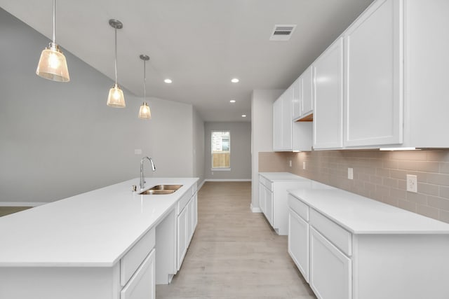 kitchen with hanging light fixtures, light wood-type flooring, sink, and a kitchen island with sink