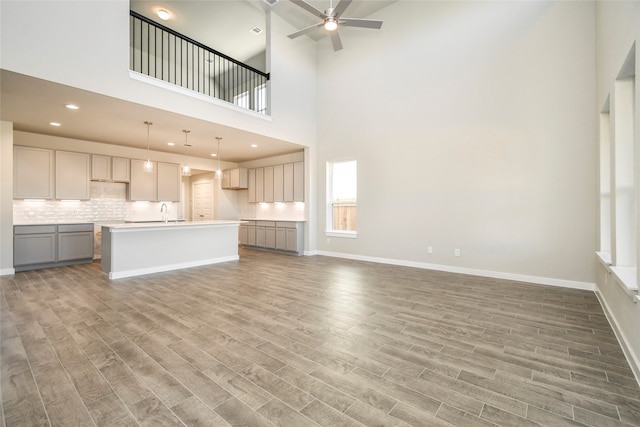 unfurnished living room with ceiling fan, hardwood / wood-style floors, a high ceiling, and sink
