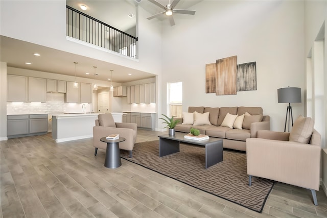 living room featuring ceiling fan, a towering ceiling, and light hardwood / wood-style floors