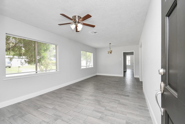 empty room with a wealth of natural light, a textured ceiling, baseboards, and ceiling fan with notable chandelier