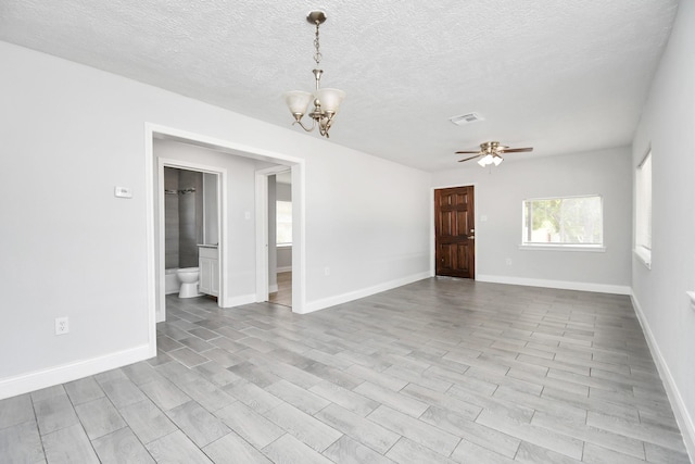 spare room with ceiling fan with notable chandelier, a textured ceiling, visible vents, and baseboards