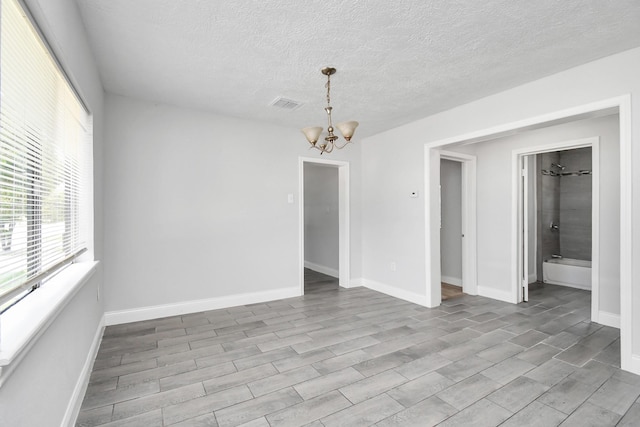 empty room featuring visible vents, a notable chandelier, a textured ceiling, and baseboards