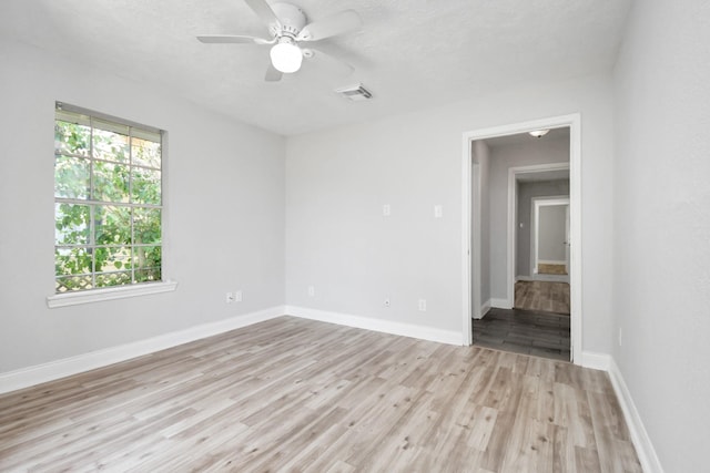 unfurnished room with light wood finished floors, a ceiling fan, visible vents, and baseboards