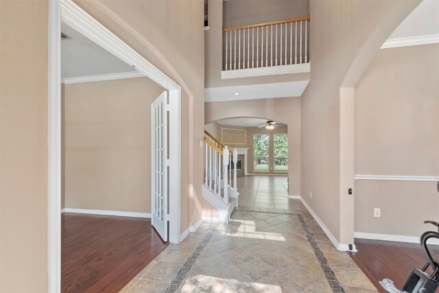 foyer entrance with ceiling fan, ornamental molding, a high ceiling, and light hardwood / wood-style floors